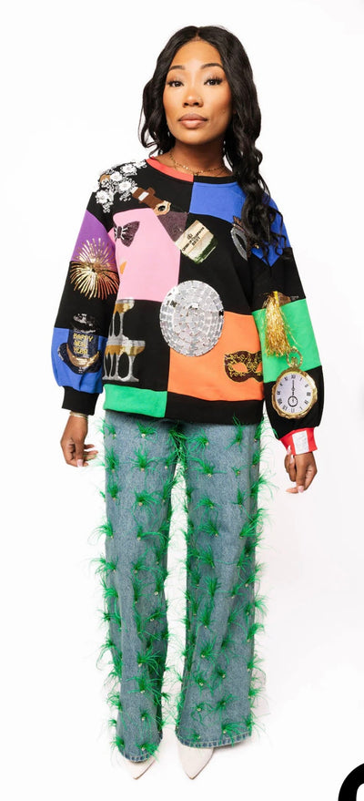 Model wearing the Queen of Sparkles Multi Checkered NYE Icon Sweatshirt with colorful patchwork and sequin New Year’s Eve icons including champagne, disco ball, and clock.